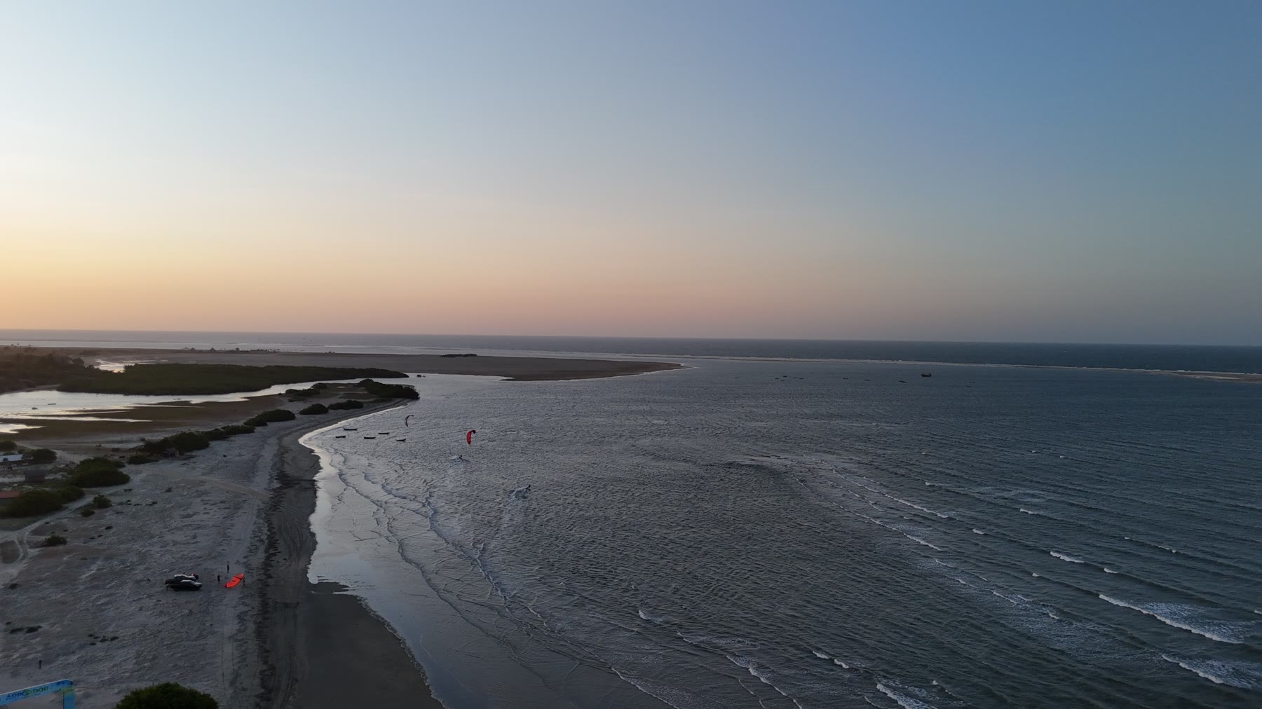 Aerial view of a beach at dusk, two red kites on the water