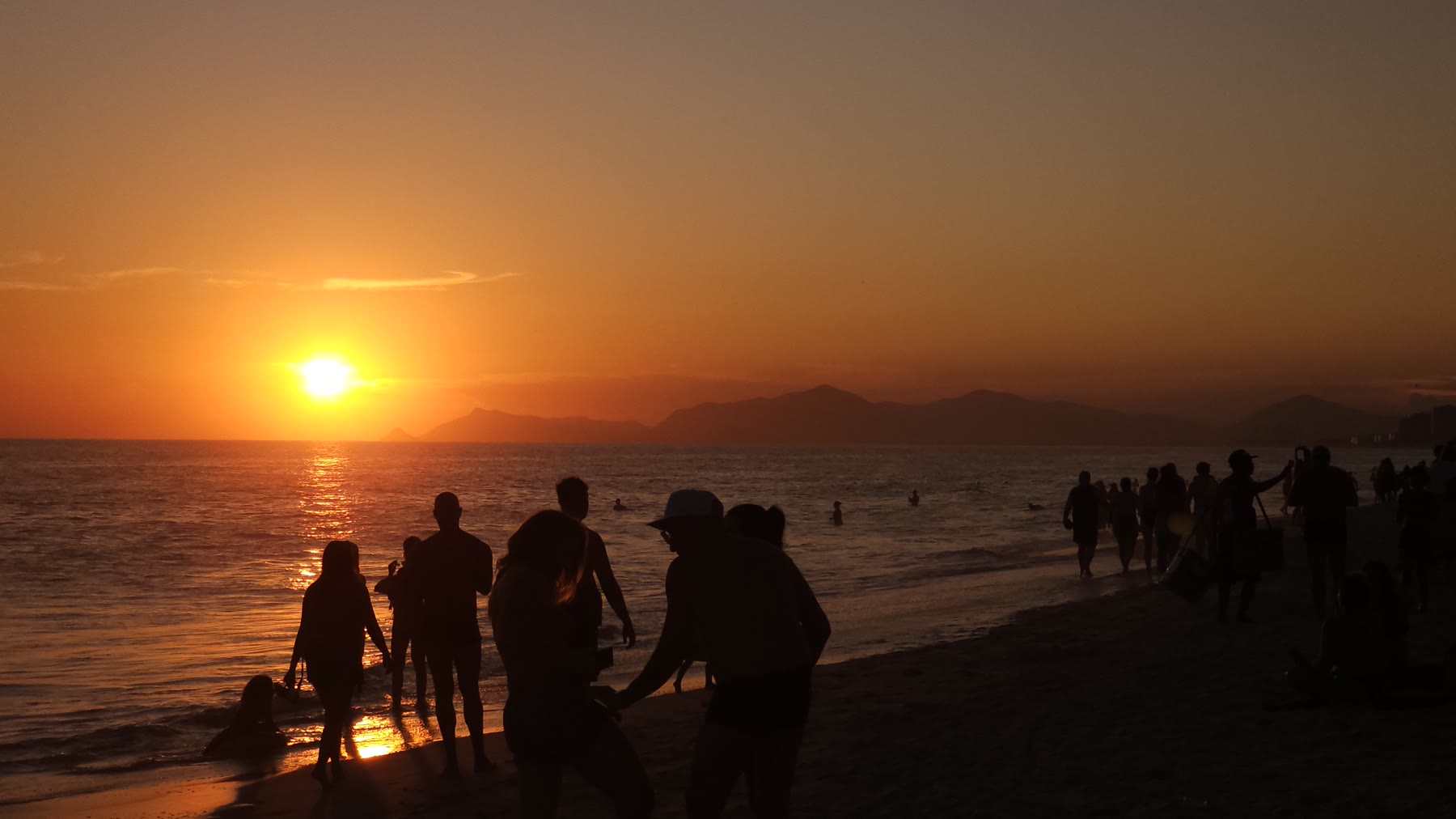 Des silhouettes sur une plage au coucher du soleil, face aux montagnes
